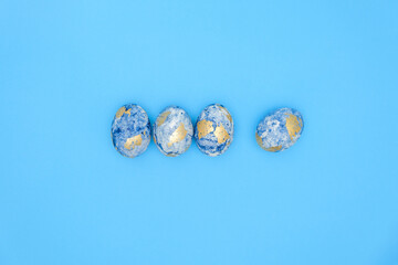 Top view of four hand-painted blue and gold eggs on a blue background. Easter concept with copy space for text. Template for greeting card, banner, wallpaper. Minimal flat lay easter style