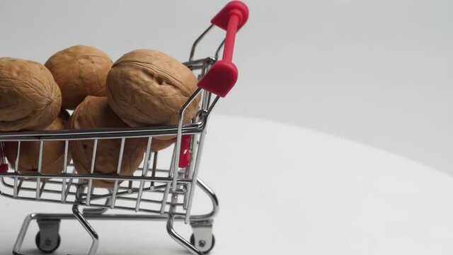 a miniature supermarket basket filled with walnuts slowly rotates on a white background. close detailed plan