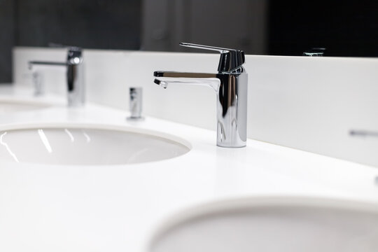 Luxury faucet mixers in a row in a modern commercial bathroom. The concept of an antivirus for sanitary prevention