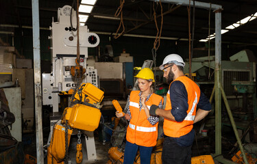 Female mechanical engineer or worker with hardhat and safety gears is working with her supervisor in a factory checking the function of a system