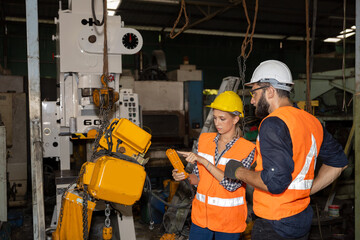 Female mechanical engineer or worker with hardhat and safety gears is working with her supervisor in a factory checking the function of a system