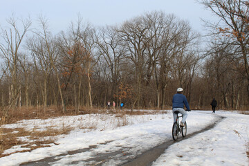 Fototapeta na wymiar Bicycle rider and four walkers on the North Branch Trail at Miami Woods in Morton Grove, Illinois in winter