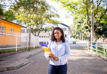 Portrait of a young college girl holding folders and notebooks and walking down the street to go to...