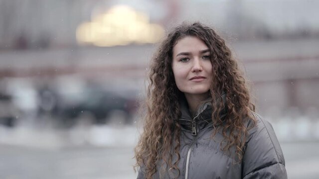young female student is walking alone in city at winter day, looking around and smiling for camera, portrait
