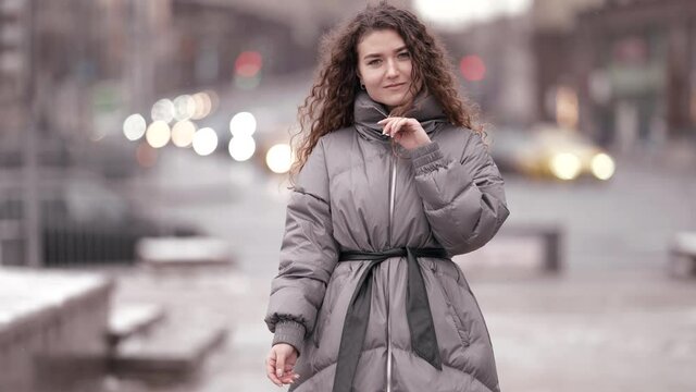 positive woman dressed down jacket is walking in city at winter day, snowless season in town