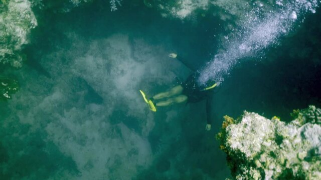 A scuba diver with yellow fins lets up a steady stream of bubbles gently treading water in a coral reef crevice - Banda, Indonesia