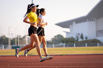 Obraz premium Two young Asian women in sports outfits jogging on running track in city stadium in the sunny morning to keep fitness and healthy lifestyle. Young women run on the stadium track. Sports and recreation