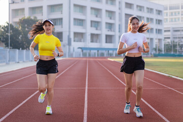 Obraz premium Two young Asian women in sports outfits jogging on running track in city stadium in the sunny morning to keep fitness and healthy lifestyle. Young women run on the stadium track. Sports and recreation