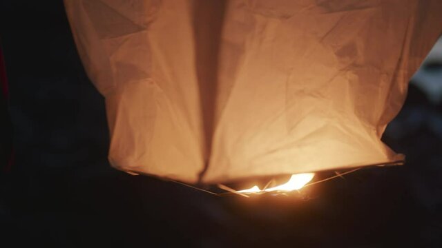 Hands turning over a paper lantern after lighting, preparing to launch
