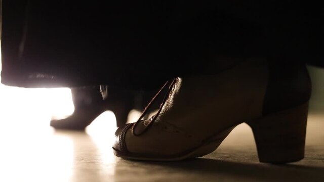 closeup of stiletto flamenco shoes and a piece of black long skirt dancing and stamping on a illuminated floor