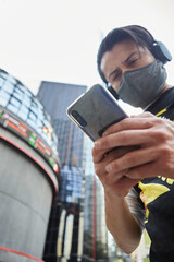 Young Hispanic man with mouth cover using his smart phone outside a stock exchange centre