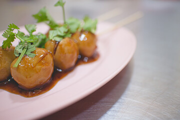Thai pork balls with brown sweet sauce on plastic dish.