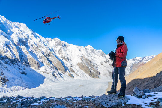 Beautiful landscape with mountains, a huge blue glacier and a silhouette of a man photographing a beautiful view against the background of mountains, a glacier and an ambulance helicopter