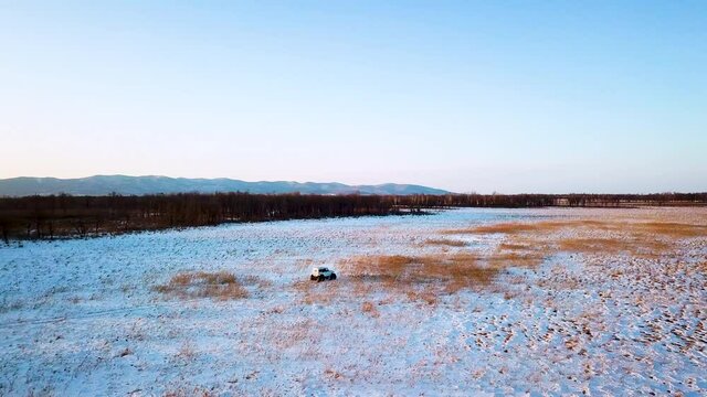 View from above. Inspector raid on a winter reserve in Russia on a swamp vehicle. A jeep on large wheels drives through a snow-covered field.