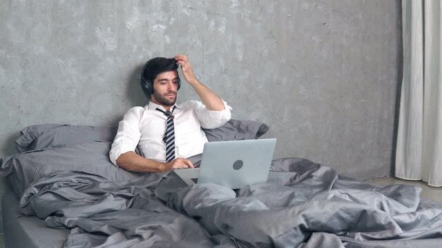 Footage B roll of Manager man in suit being in business trip lying on bed in hotel room and speaking online using laptop. Startup business concept. Business relaxing concept. Watching movies.
