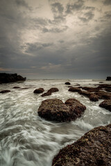 Obraz premium Beautiful seascape for background. Beach with rocks and stones. Low tide. Motion water. Cloudy sky. Slow shutter speed. Soft focus. Copy space. Vertical layout. Mengening beach, Bali