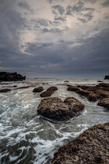 Fototapeta na wymiar Beautiful seascape for background. Beach with rocks and stones. Low tide. Motion water. Cloudy sky. Slow shutter speed. Soft focus. Copy space. Vertical layout. Mengening beach, Bali