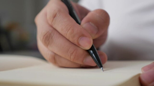 Close up of hand holding pen and writing on empty book paper