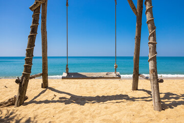 Naklejka na ściany i meble The wooden swing is right on the beach with a clear sea and blue sky in the background. Concept about resort, travel, nature, landscape, health. No people
