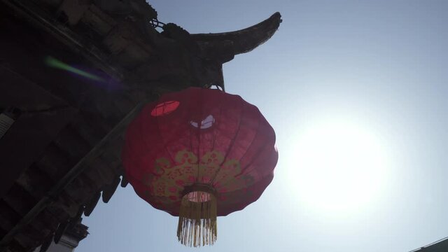 Panning shot of red Chinese lantern hanging from roof against clear blue sky on sunny day - Suzhou, China
