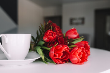 Bouquet of red tulips on table and white coffee cup. Concept for greeting card