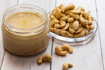 A jar of cashew butter with a bunch of fresh cashew on a white wooden table. Homemade cashew butter, natural, healthy food. The modern wellness and vegan concept.