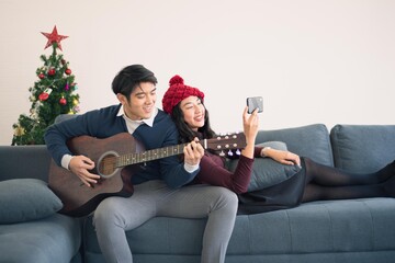 Asian man and woman couple family in casual outfit holiday winter theme live together and playing music guitar with happy and romantic in modern living room