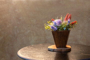 Colorful artificial flowers in a wood vase  on  table with cement wall background