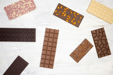 different sweet, delicate chocolate bars lie creatively on a white wooden background