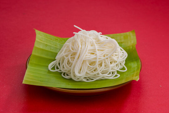 Ideyappam or  noolappam arranged in a fresh green banana leaf with red textured background.