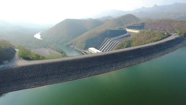 Aerial view, drone move forward - A reservoir next to hydroelectric power station dam with mountain background on a sunny day.
