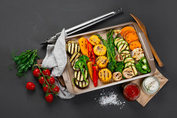 Grilled assorted vegetables in beige tray on black background.