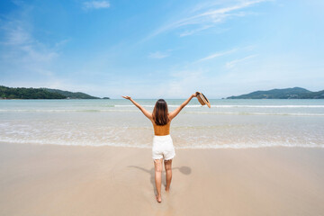 Young woman traveler relaxing and enjoying at beautiful tropical white sand beach with wave foam and transparent sea, Summer vacation and Travel concept