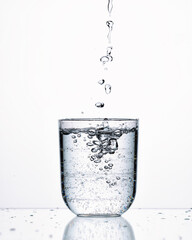 pour mineral water into a glass, on a white background with splashes and gurgles