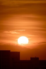 large round orange sunrise or sunset over city with texture of cloudy sky for background, big and powerful sun shot with super telephoto lens