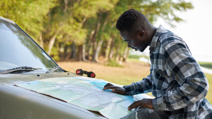 A black man was looking at a map to find a route in front of the car.