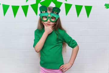 Portrait of a surprised, brooding Caucasian girl in a green T-shirt wearing clover leprechaun...