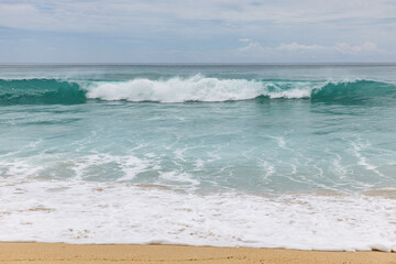 Seascape background. Sandy beach, milky foam waves, blue ocean. Scenic waterscape. Horizon line. Cloudy sky. Nature and environment concept. Daylight. Copy space. Dreamland beach, Bali