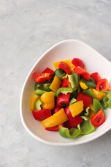 Fresh raw yellow, green, red bell peppers, and onions placed in a white bowl. Diced colorful capsicum. chopped colorful veggies for Chinese preparation. Healthy vegetable background with copy space.