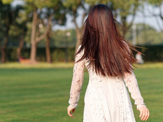 Rear view of beautiful Chinese young woman in white dress running with her shining black long hair in sunny day.
