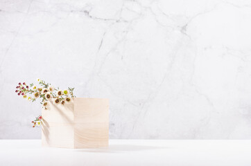Wooden cube podium with twig of white spring flowers in white and grey marble interior with sun...