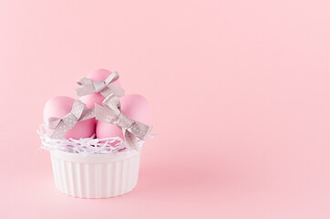 Sweet easter background -  pink easter eggs with silver bow in white ceramic bowl on pastel pink color.