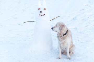 White Golden Retriever Standing Next to a Snowman in the Snow