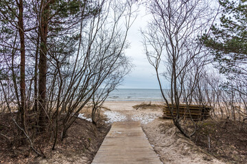 Fototapeta na wymiar Wooden Path to a Frozen Baltic Sea Coast in Late Winter on a Cloudy Day