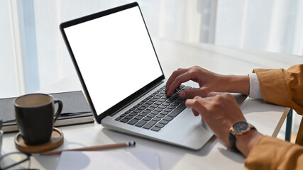 Close up view of man hands typing on keyboard of laptop computer on white desk at his home office.