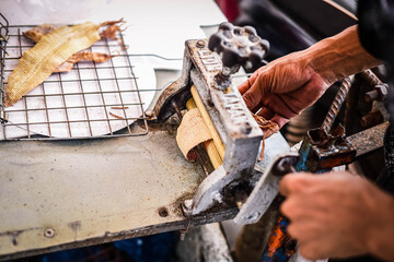 
A dried fish merchant grinds dried squid with hand-cranked uniforms on a cart on the beach of...