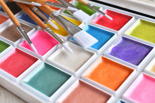 A close up image of a brightly colored set of water color paints with paint brushes.  