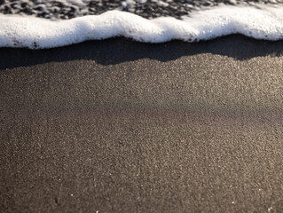 Wave close up on black sand beach. Waterscape background. Selected art focus. Black sand beach with white milky foam waves. Nature and environment concept. Black and white contrast.