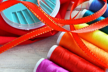 A top view image of brightly colored thread with sewing needles and a pair of scissors. 