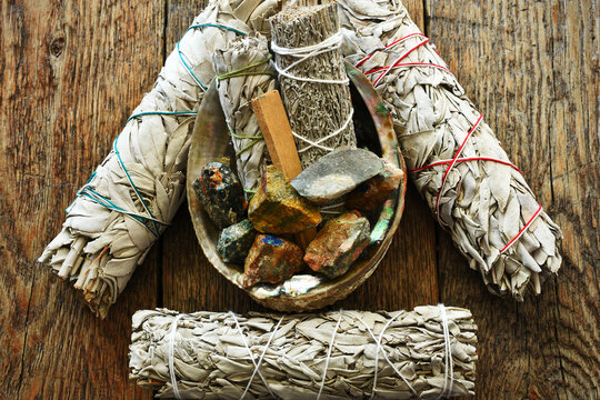 A close up image of several raw healing crystal and white sage smudge bundles. 